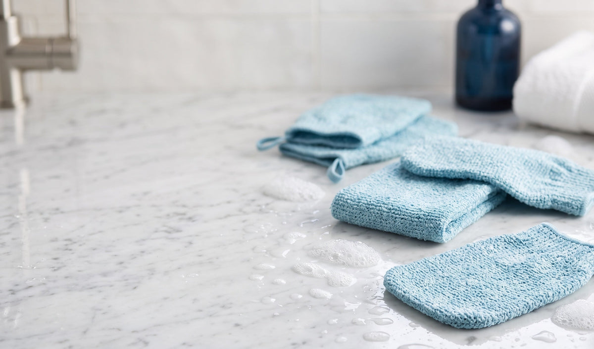 Korean viscose exfoliating mitts arranged on a marble bathroom counter