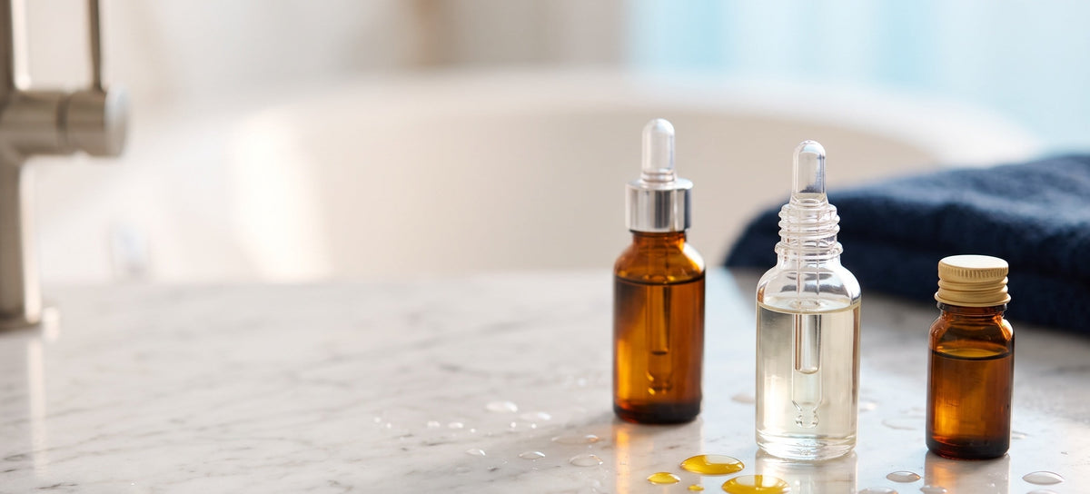 Amber and clear glass dropper bottles of after-bath oil on a marble counter